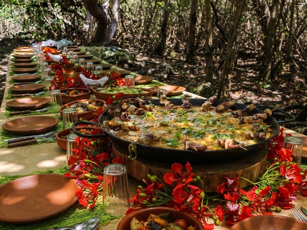 A mesa longa sob o cajueiro, com a paella no centro e flamboyant